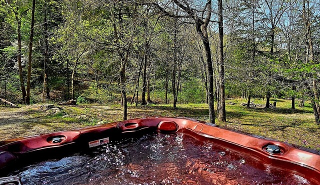 Escape to Whispering Hollow, a peaceful retreat near Eureka Springs with a dreamy glass room, cozy indoor spaces, and a brand-new hot tub for unwinding under the trees and surrounded by nature.